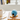 Blue birdhouse-shaped object on a wooden surface with a cup of coffee and cookies.